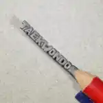 Inscription « Taekwondo » à l'horizontale - Mot « TAEKWONDO » en lettres majuscules en relief, disposées horizontalement.